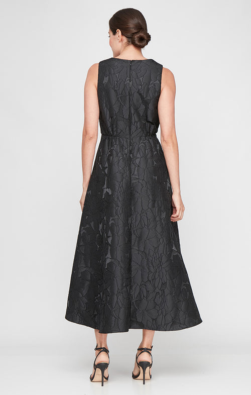 Woman wearing a black sleeveless dress with a subtle pattern on a white background